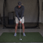 Golfer practicing a wedge pre-shot routine at home before making a calm training swing.