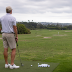 Experienced golfer finishing a wedge range session, looking from a neat cluster of balls toward a distant course-like target, reflective posture.