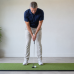 Golfer building a balanced putting setup at home with relaxed hands and square putter face.