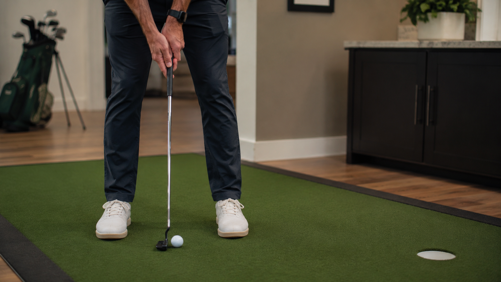Golfer building a balanced putting setup at home with relaxed hands and square putter face.
